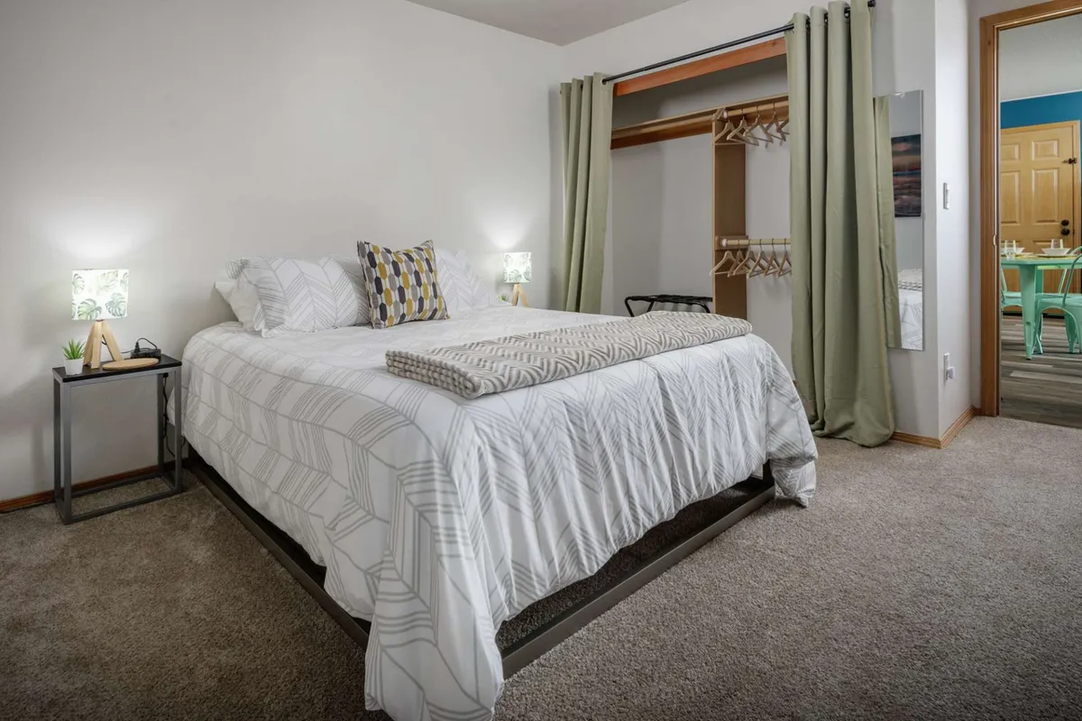 This image shows a bedroom with a plush queen bed adorned with decorative pillows, flanked by nightstands and a closet area in view. The room feels warm and inviting, ideal for unwinding after a day of exploration.