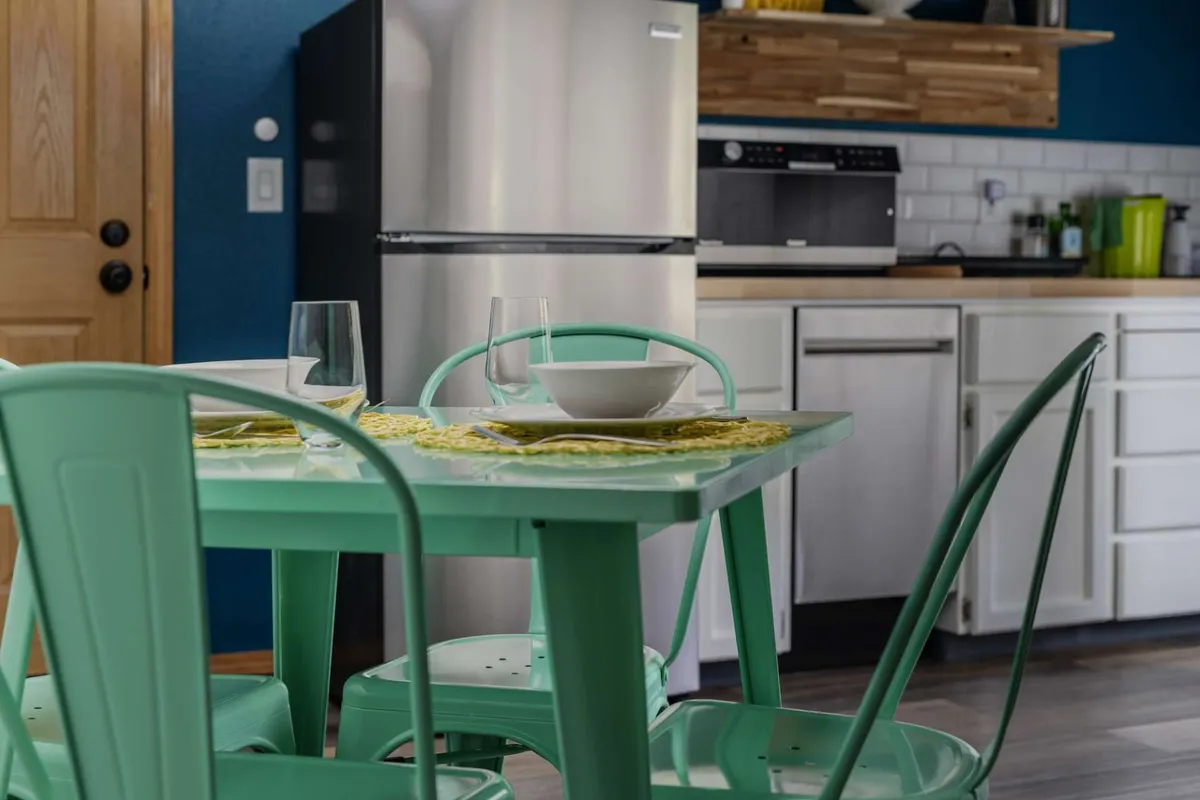 A cheerful dining area with a mint green table and chairs, set with a white bowl and glassware. The arrangement evokes a sense of togetherness and casual dining, perfect for shared laughter and family-style meals.
