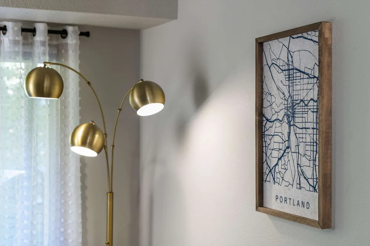 A cozy living area featuring a comfortable chair positioned under a floor lamp, with a prominent map of Portland displayed on the wall. The warm, inviting setup suggests a space for relaxation, reading, and reflecting on the day's explorations in the city.