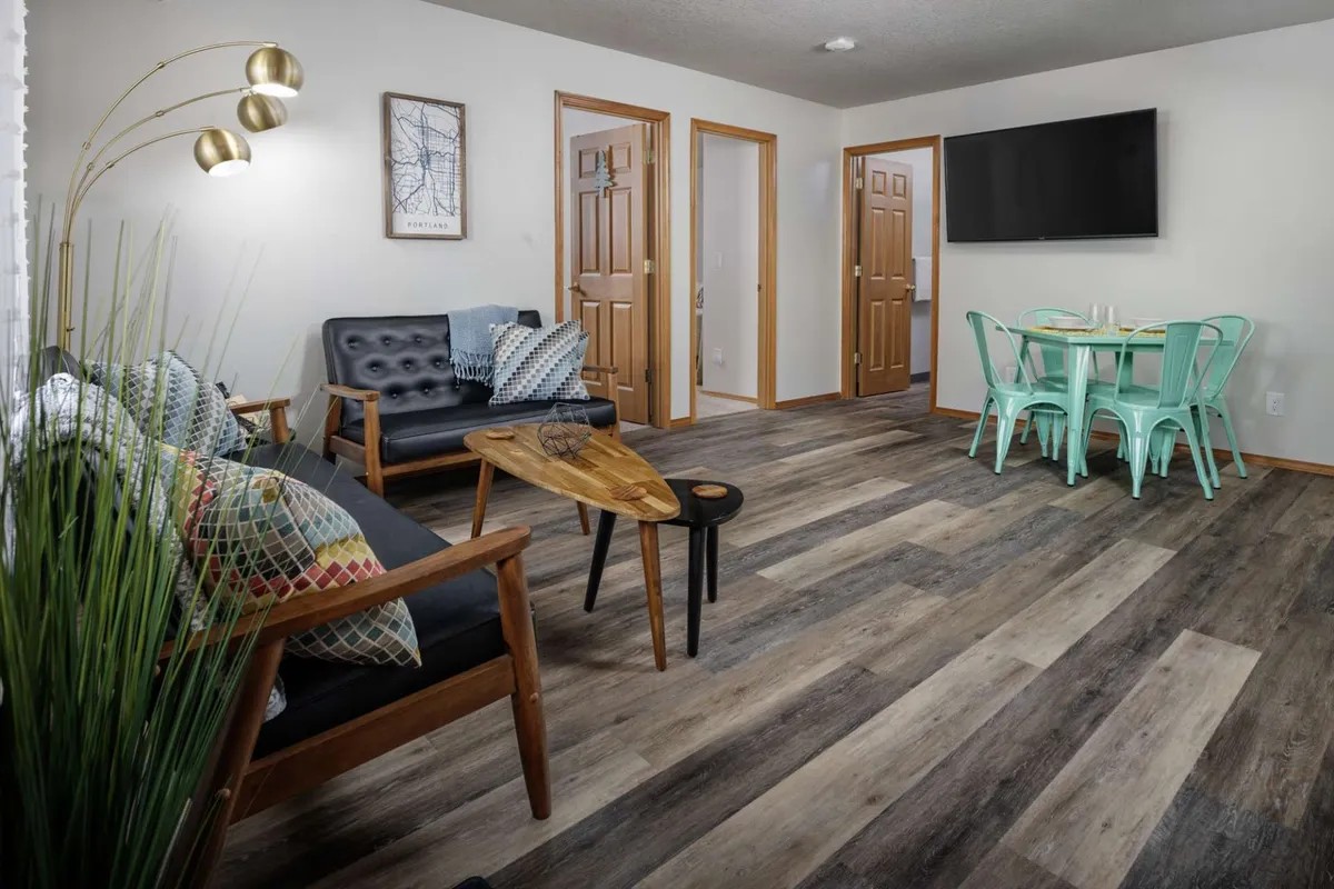 A view of a cozy and modern open-plan living space, featuring a comfortable sofa, a dining table set, stylish decorative art on the walls, and sleek flooring. The layout showcases a seamless flow between lounging and dining areas, ideal for relaxation and group gatherings.