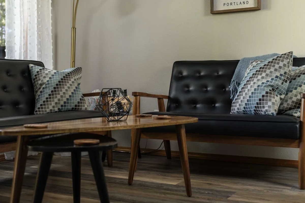 This interior scene showcases black leather sofas with geometric cushions, a wooden coffee table, and a contemporary, relaxed atmosphere. The space suggests comfort and privacy, ideal for unwinding independently yet offering enough space for occasional friendly encounters with owners.