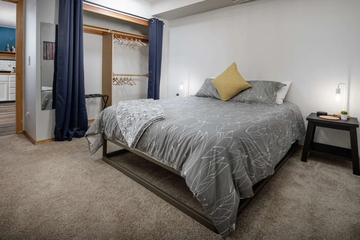 This image reveals another serene bedroom featuring a queen bed with decorative pillows, a cozy nightstand with a lamp, and an inviting atmosphere flooded by natural light. The space exudes calm, supporting personal rest and downtime.