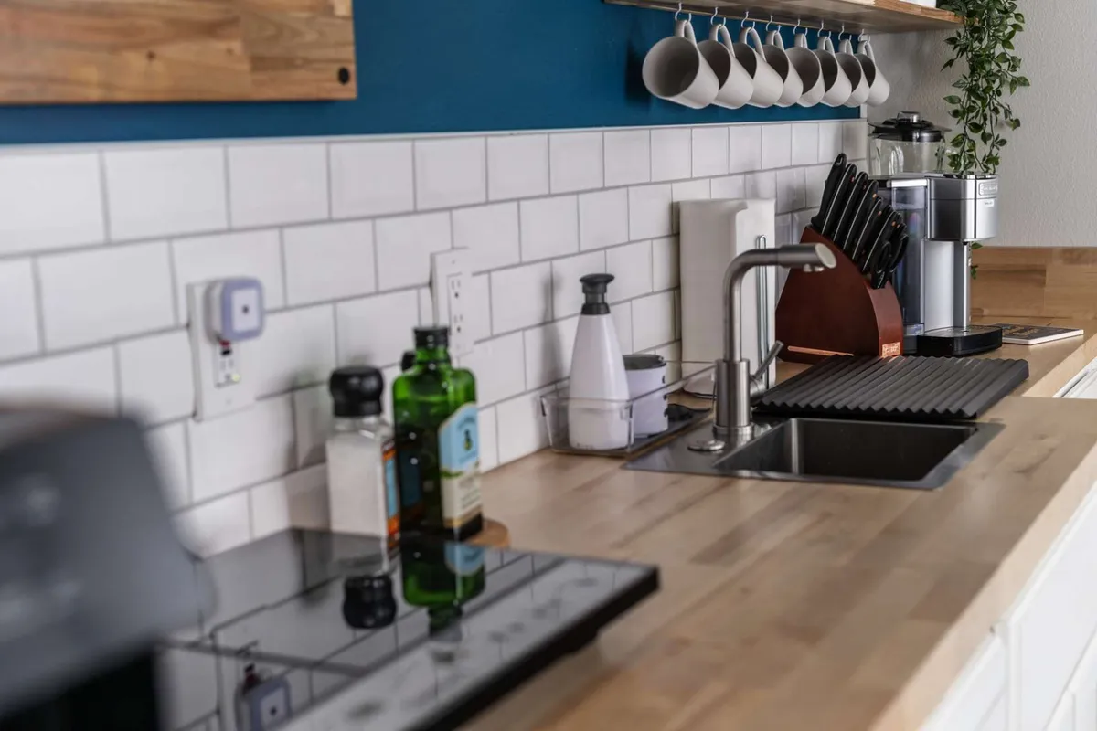 A close-up of a fully equipped kitchenette, including a kitchen sink, countertop with kitchen utensils, spice bottles, and a coffee maker. The space feels warm and welcoming, designed for both meal prep and casual socializing.